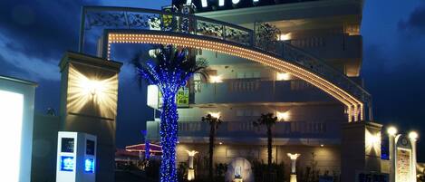 Entrada de hotel con un letrero de neón, una palmera iluminada con luces azules y un cartel.