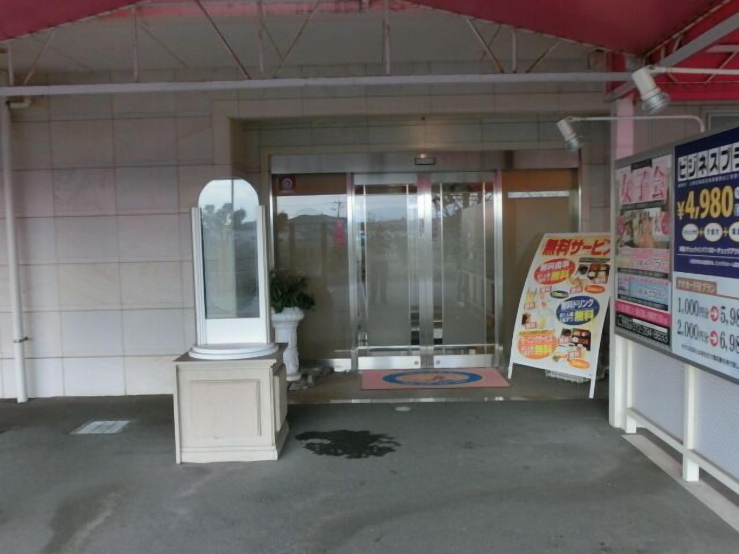 Ingresso di un hotel con porta in vetro, un pilastro bianco e un tendone rosso.