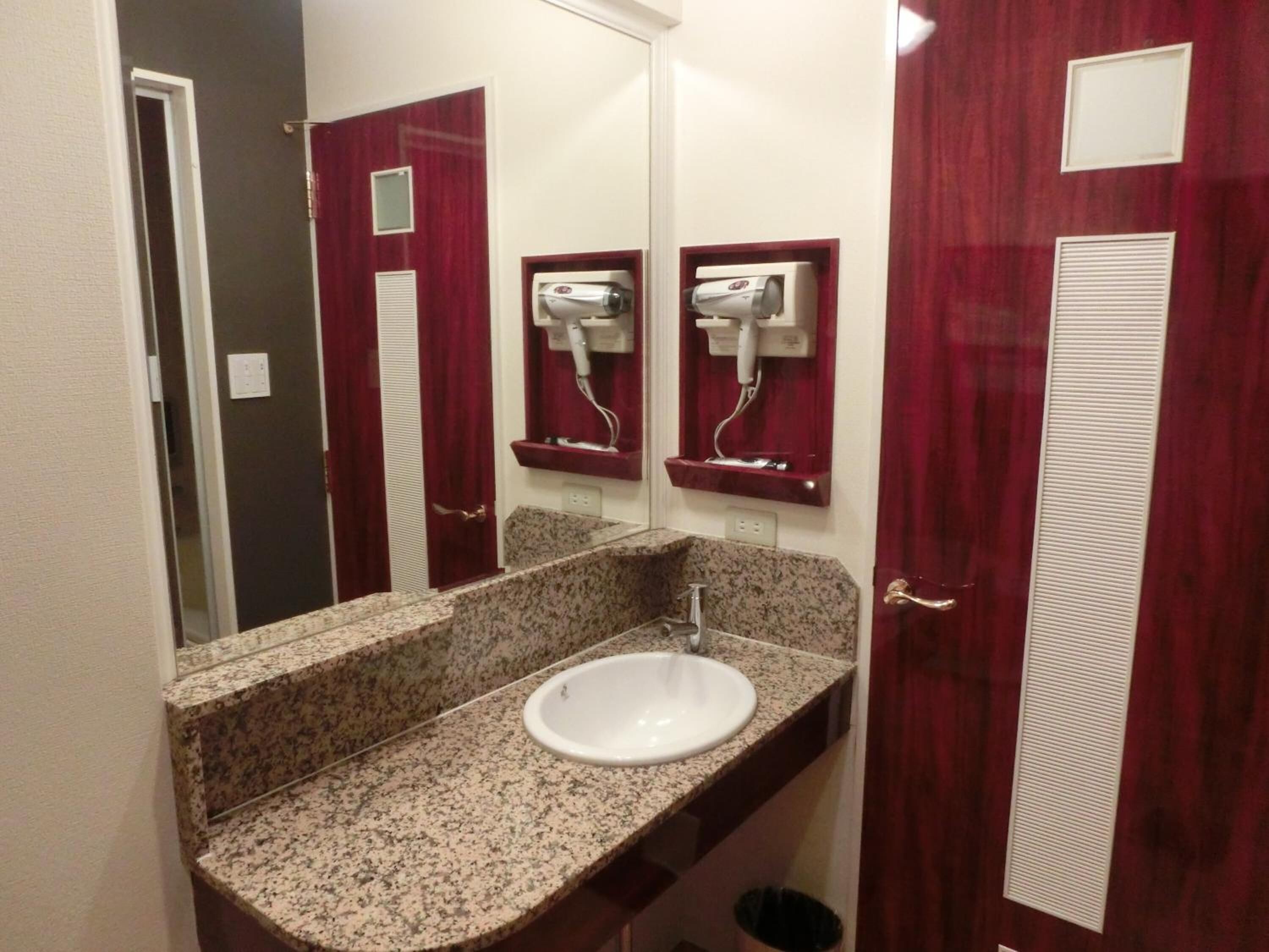 A bathroom with a granite countertop sink, a mirror, and a red door.