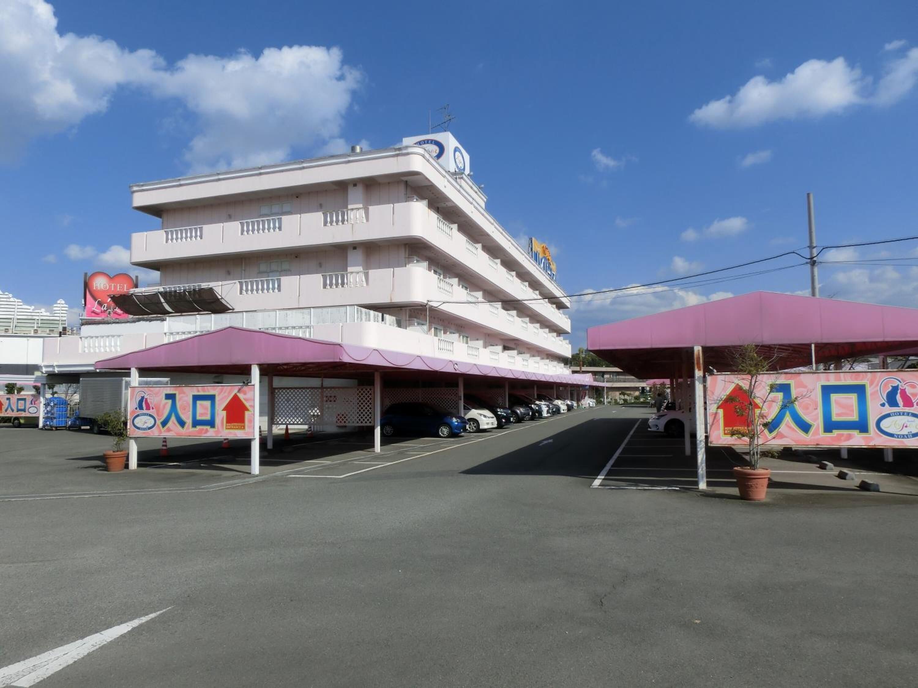 Un hotel de varios pisos con un llamativo letrero que dice 'HOTEL', un área de estacionamiento techada y un cielo despejado.
