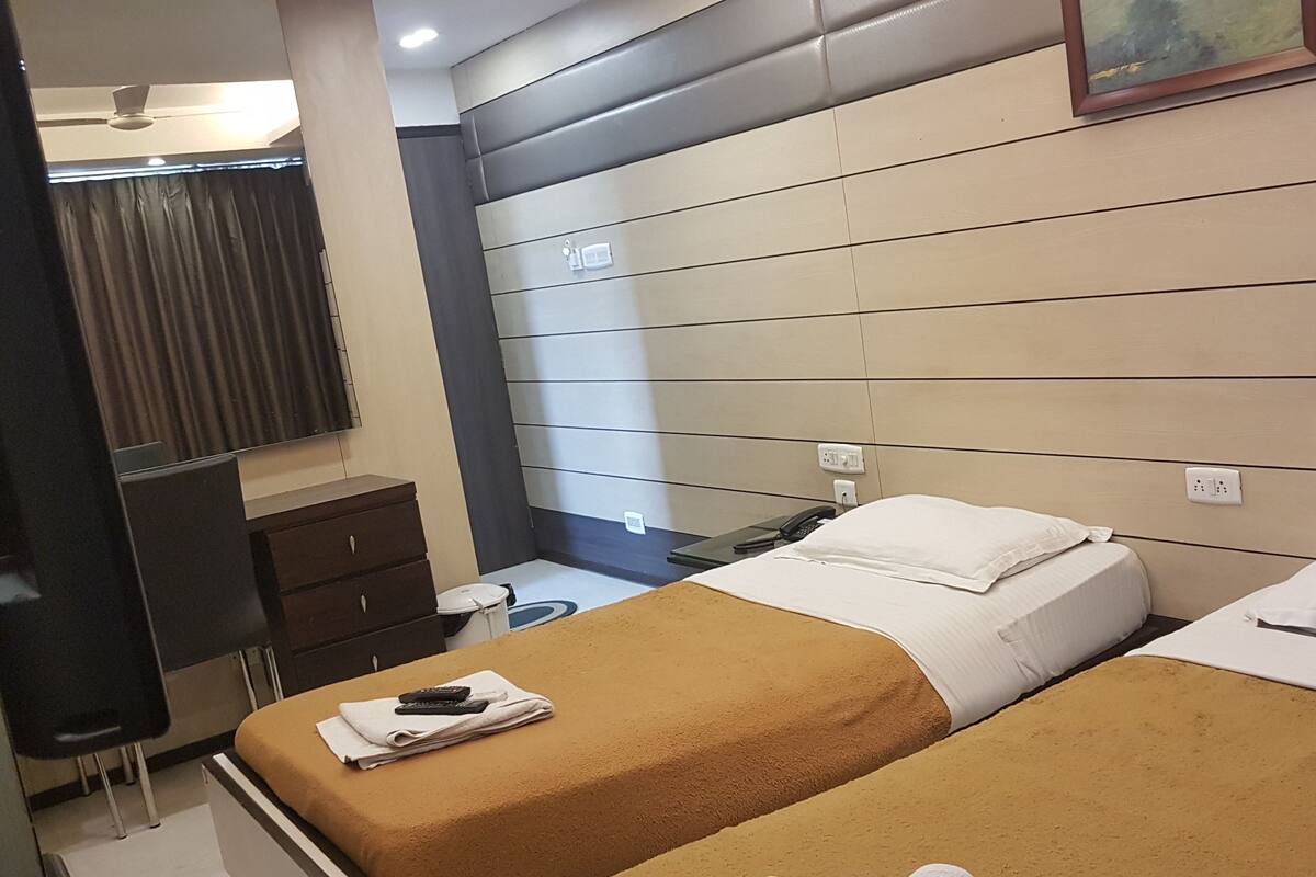 A hotel room with two beds, a desk, a chair, a mirror, and a ceiling fan.