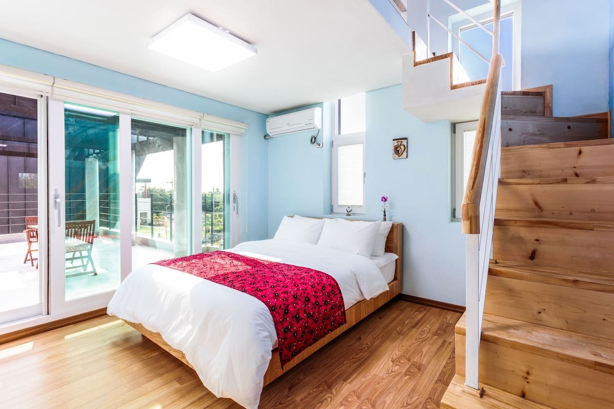 Un dormitorio con cama, una escalera de madera y un ventanal corredero que da a un espacio exterior.