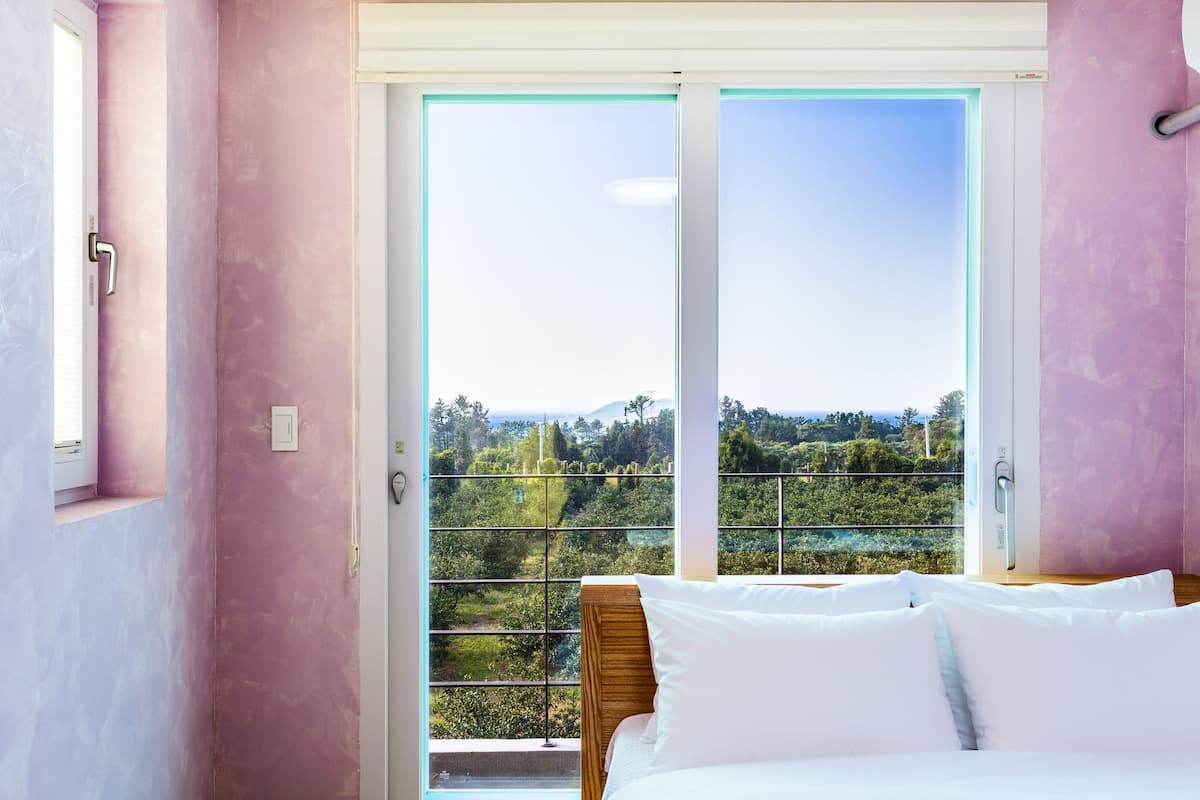 Un dormitorio con cama, ventana con vista a follaje y puerta corrediza.