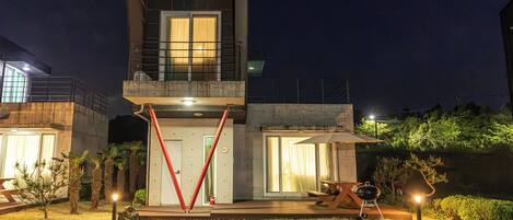 A modern two-story building with a balcony, large windows, and a well-lit entrance.