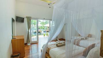 A bedroom with two beds, a wooden desk, a television, and a large window with curtains.