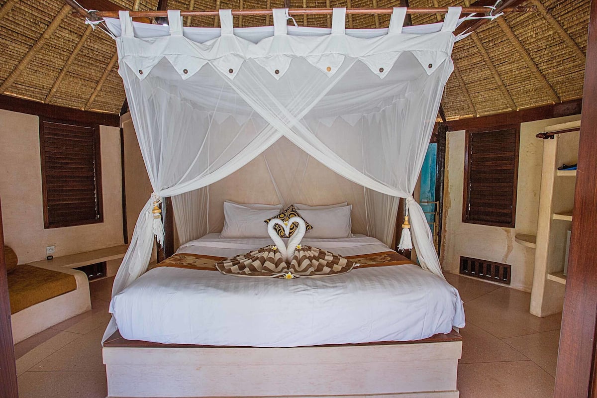Een bed met hemelbed, kussens en een decoratief zwanendesign op het beddengoed.