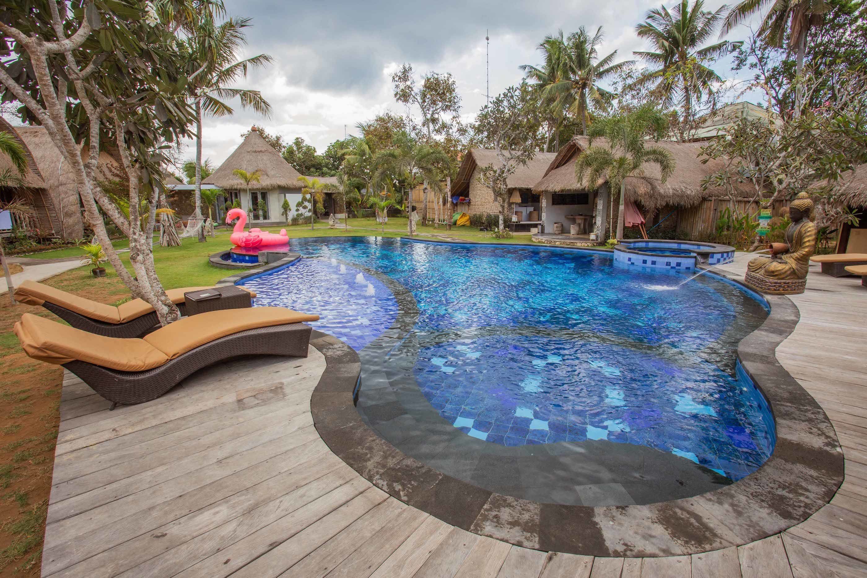 A swimming pool with lounge chairs, a flamingo float, and thatched-roof huts in a tropical setting.