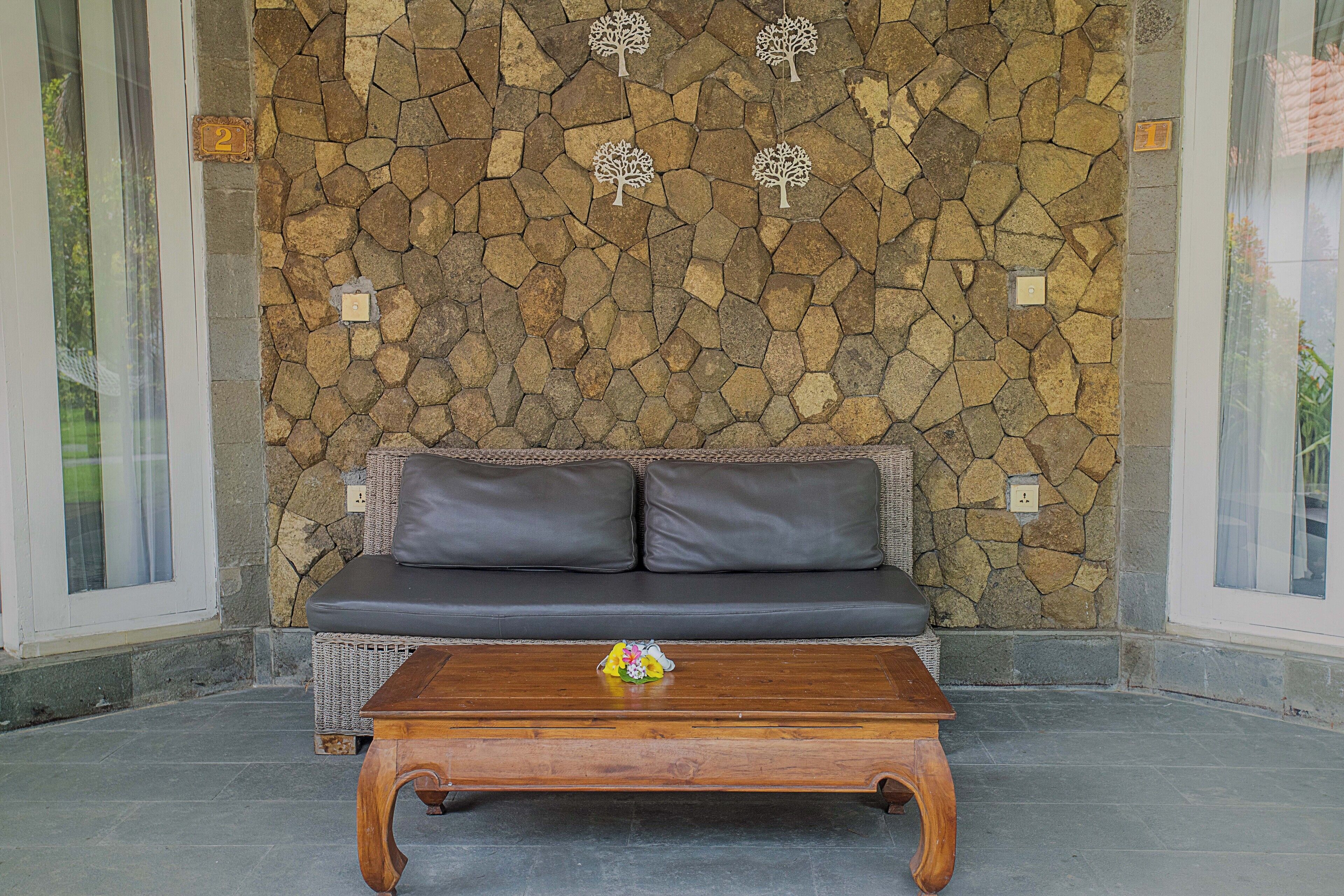 A stone wall with three tree decorations, a gray sofa with two cushions, and a wooden coffee table with a small decorative item.