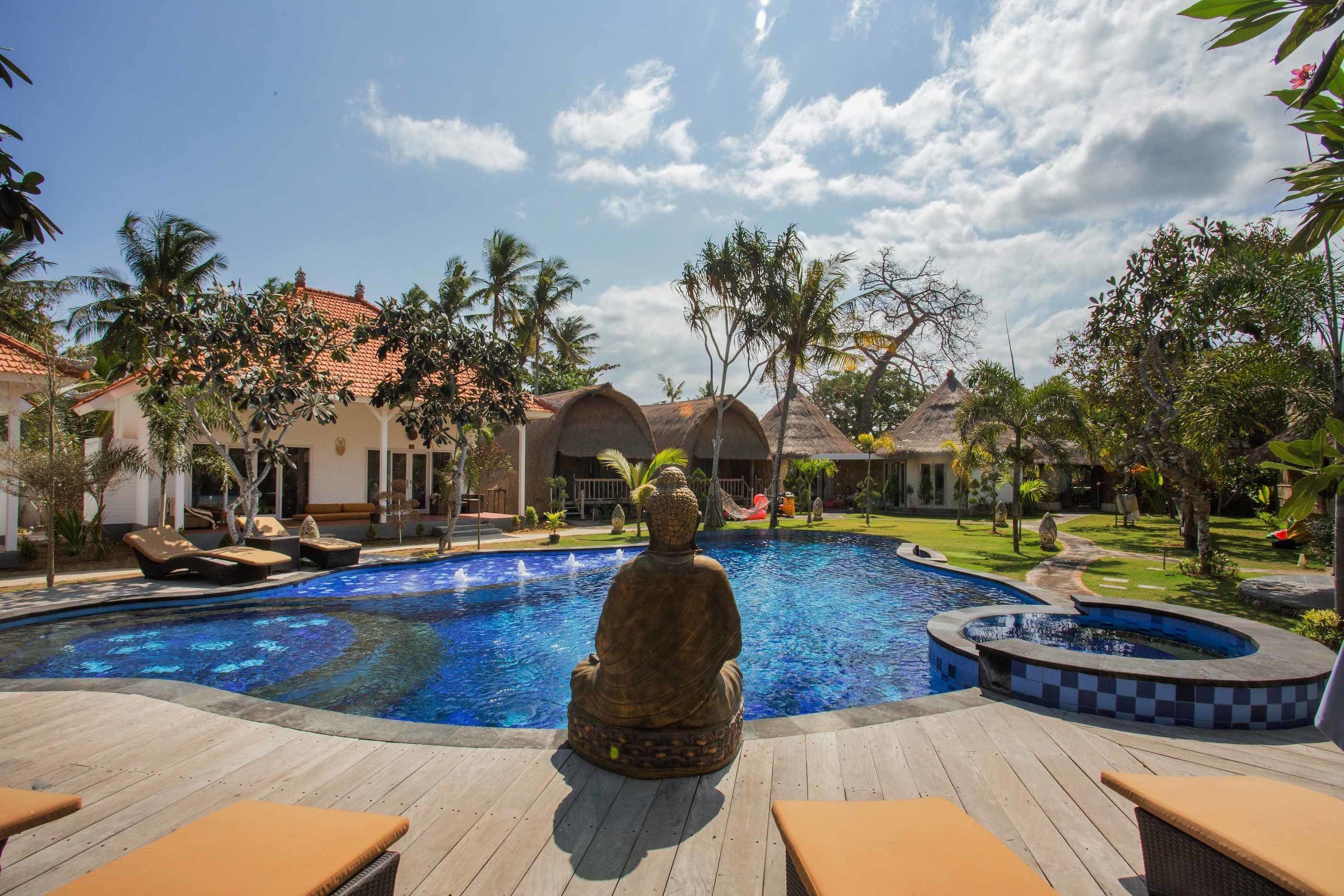 Un espace piscine agrémenté d’une statue de Bouddha, de chaises longues et d’un jardin tropical.