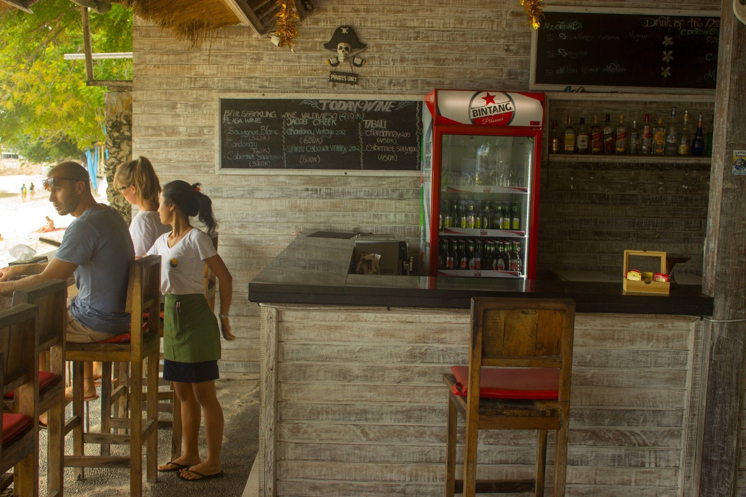 A bar area with wooden furniture, a Bintang refrigerator, and a chalkboard menu.