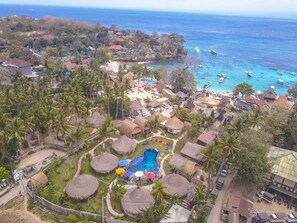 Luchtbeeld van een resort met rieten hutten, een zwembad en een strandgebied.