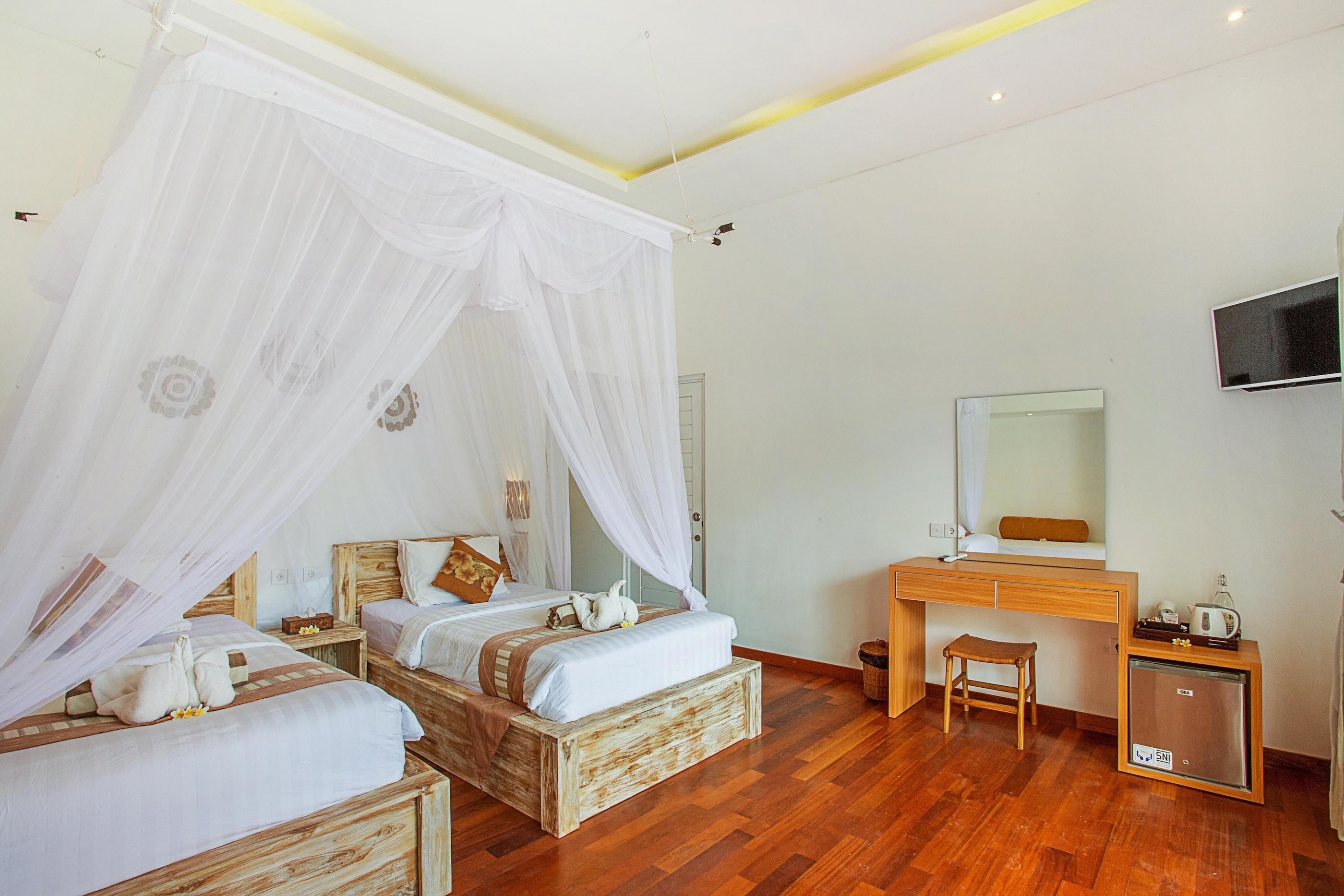 Un dormitorio con dos camas de madera, un escritorio de madera, un taburete pequeño, un televisor y un refrigerador.