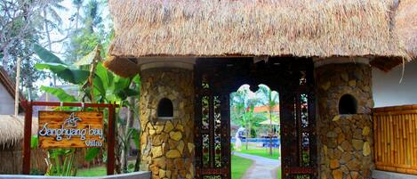 Una entrada con arco de piedra y techo de paja que conduce a un edificio con el letrero 'Sanghyang Bay Villas'.