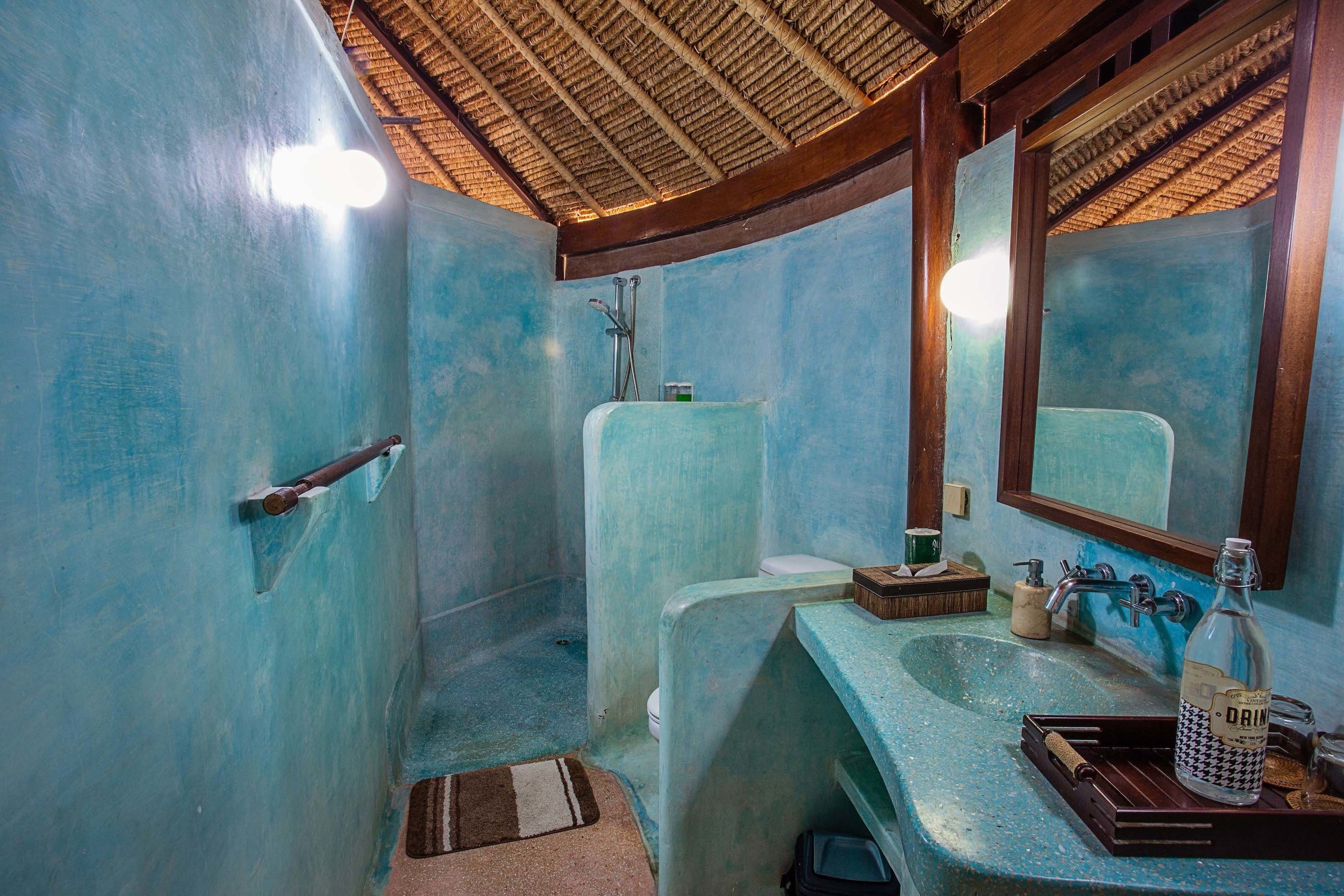 A bathroom with a blue color scheme, a shower, a sink with a bottle of drink, and a mirror.