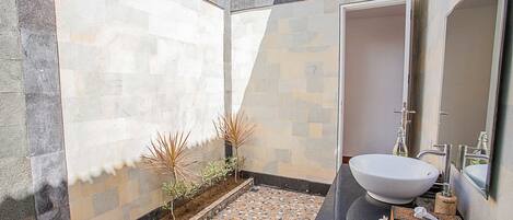 Un baño con un lavamanos grande de color blanco, un espejo y suelo de baldosas.