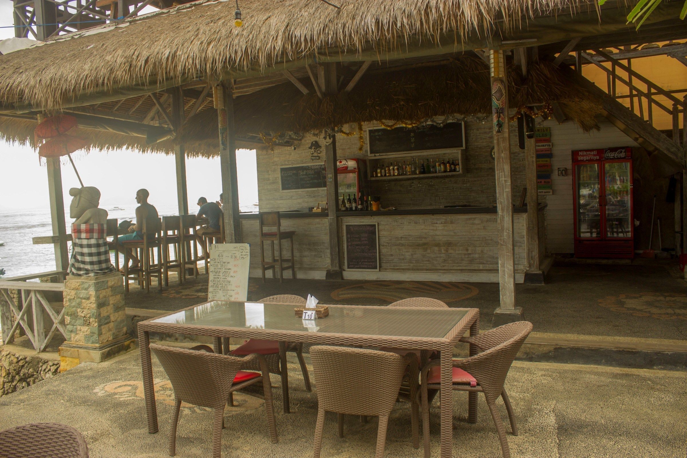 Un área de bar al aire libre con mobiliario de mimbre y techo de paja.