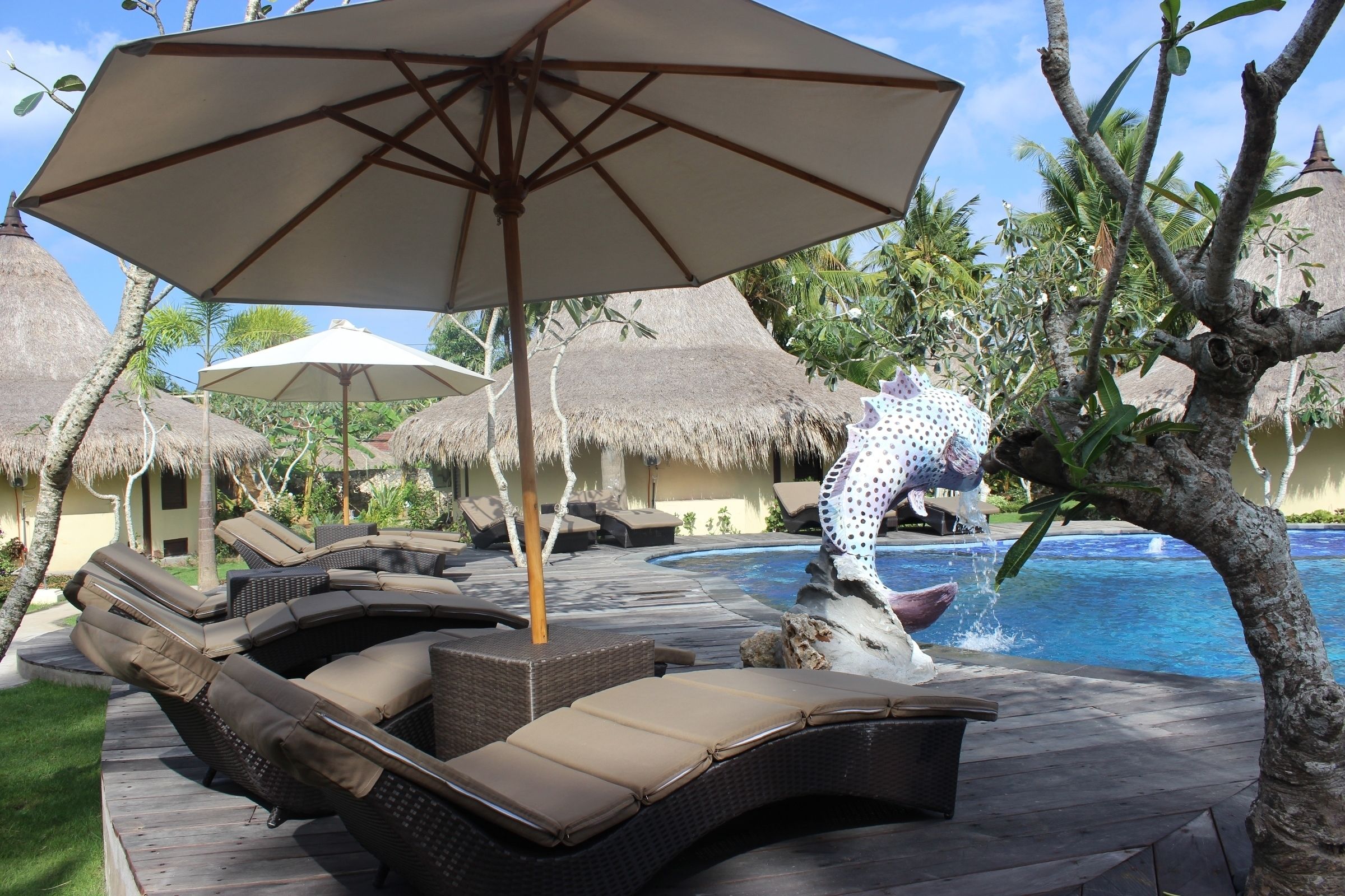 Een zwembadgedeelte met ligbedden, parasols en een decoratieve waterattractie.