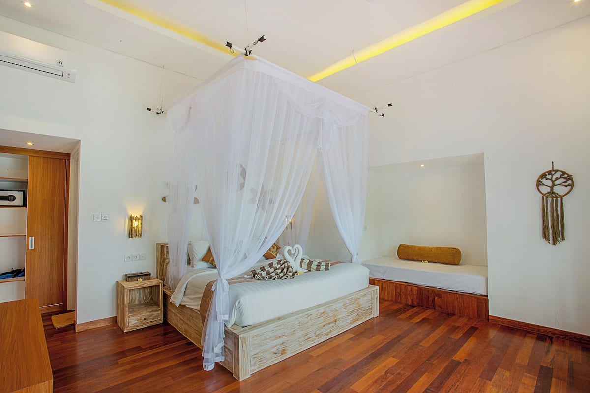 Een slaapkamer met een hemelbed, nachtkastje, bankje en een aan de muur bevestigde dreamcatcher.