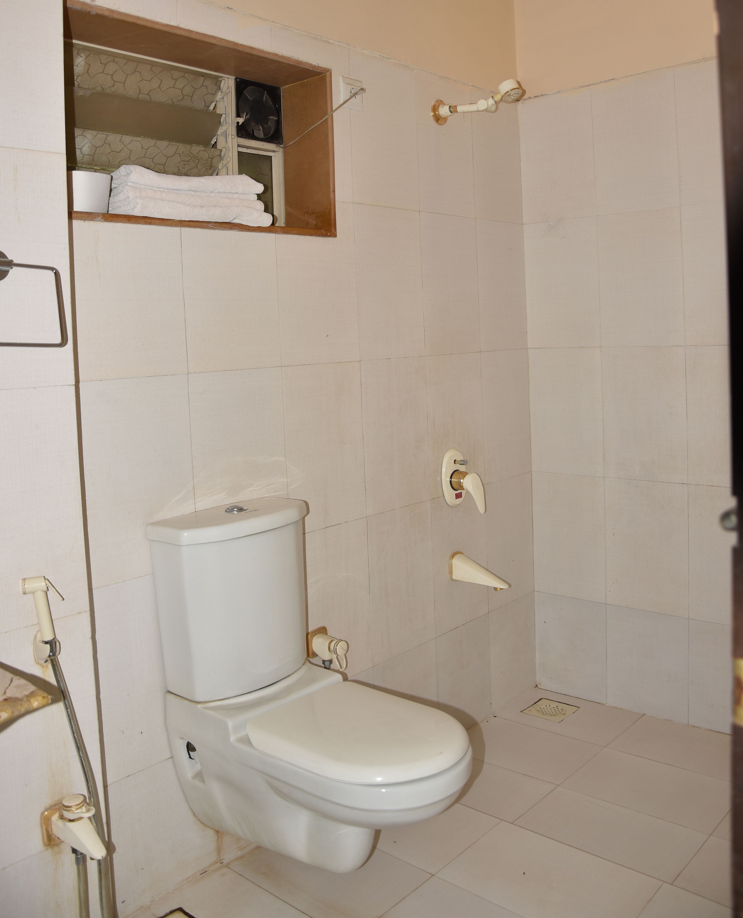 A bathroom with a toilet, a shower, and a shelf above the toilet.