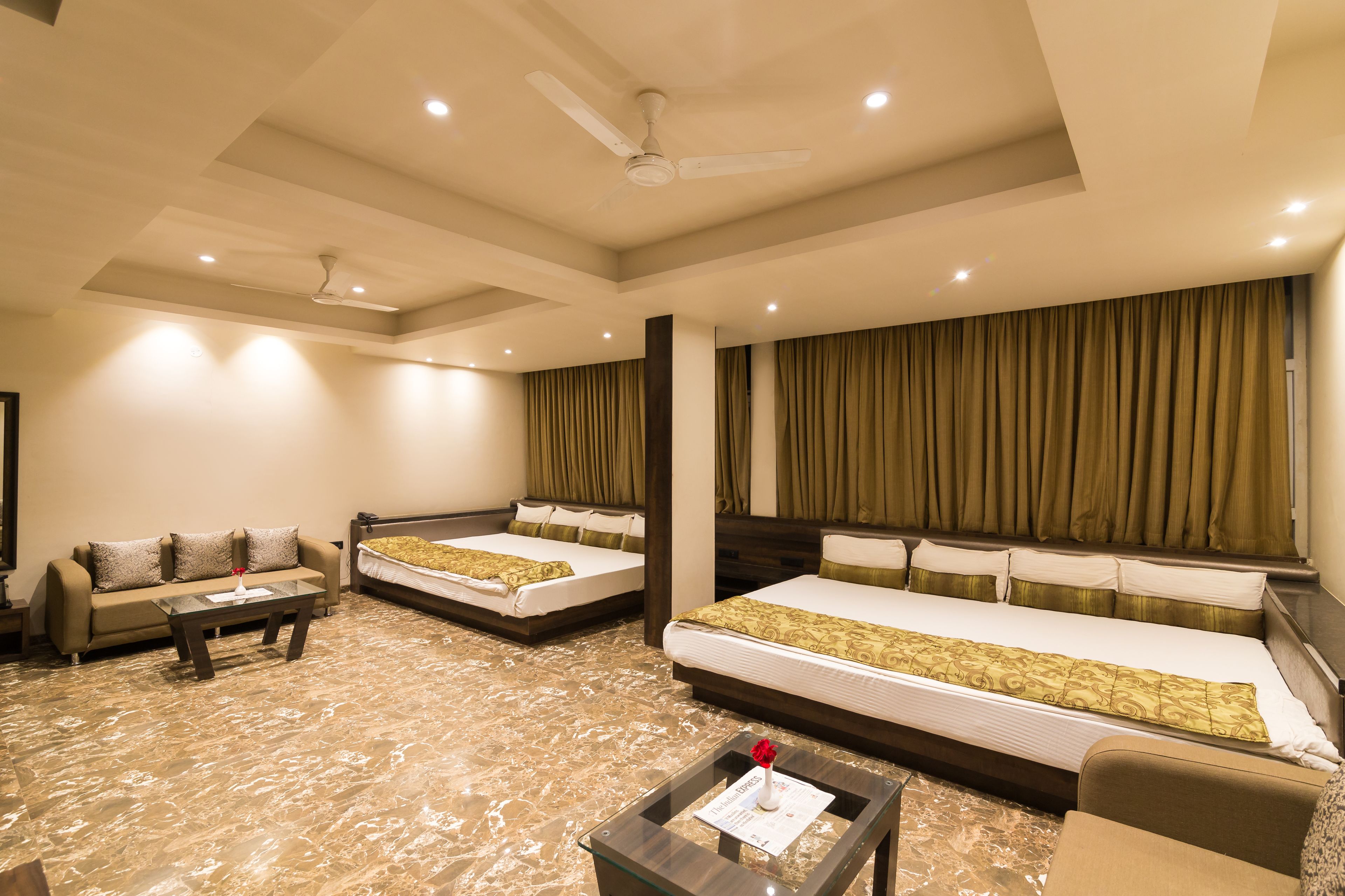 A hotel room with two single beds, a sofa, a coffee table, and a ceiling fan.