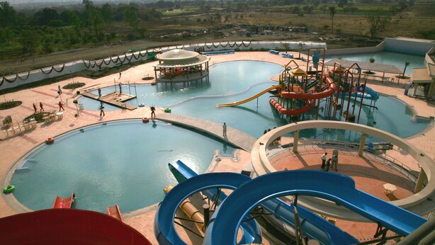 A water park with multiple pools, slides, and a large red slide. - Sentosa Resorts and Water Park (Pune)