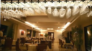 A restaurant with multiple dining tables, chairs, and hanging wine glasses. - Sentosa Resorts and Water Park (Pune)
