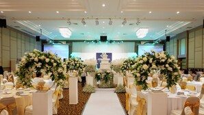 A banquet hall with white tables, gold sashes, and floral centerpieces. - The Impress Nan Hotel (Nan)