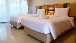 A hotel room with two beds, a large window with sheer curtains, and a wall-mounted light fixture. - The Impress Nan Hotel (Nan)