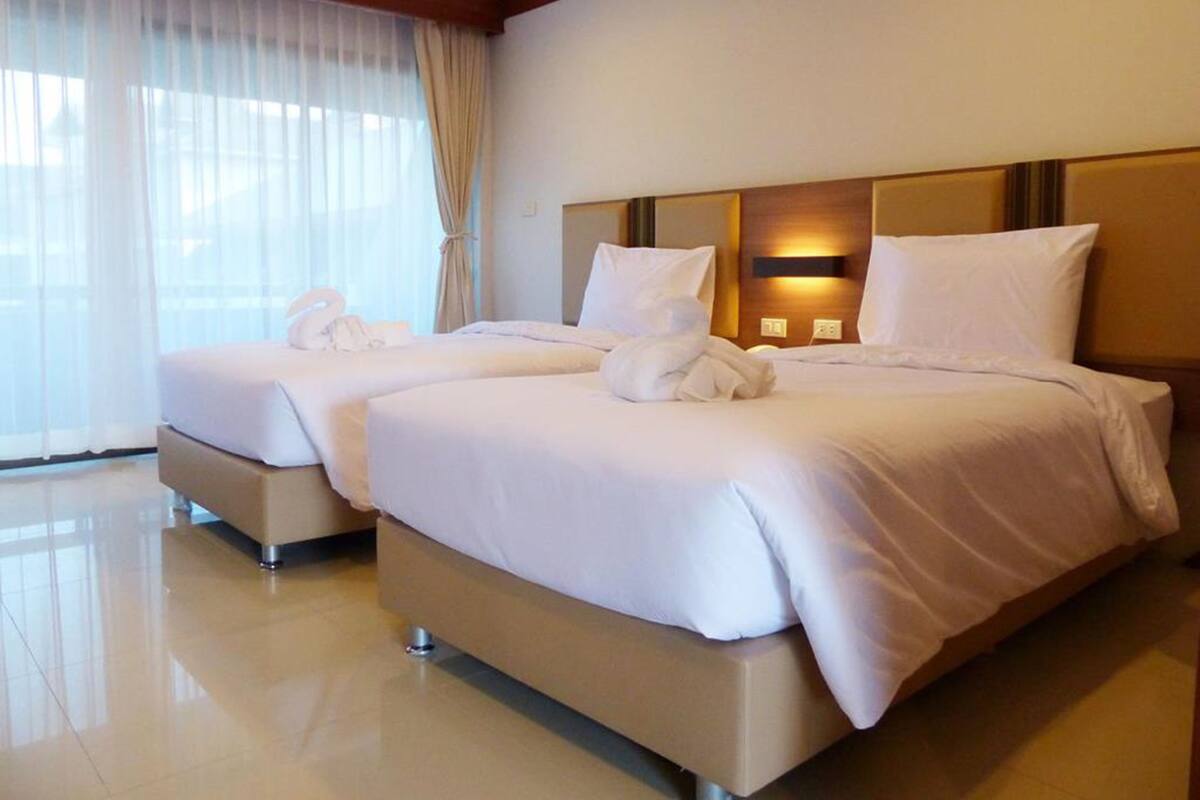 A hotel room with two beds, a large window with sheer curtains, and a wall-mounted light fixture.