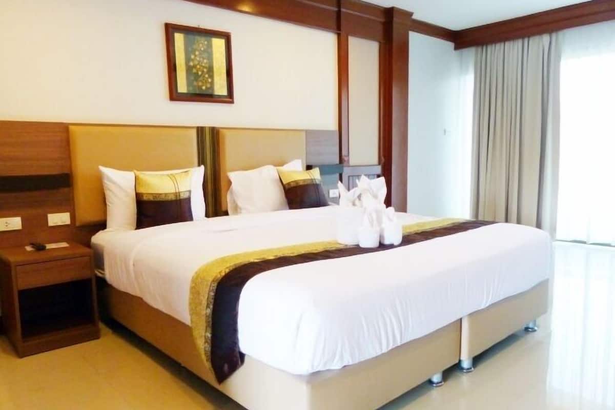 A large bed with white and brown bedding, a wooden headboard, and a bedside table with a lamp.