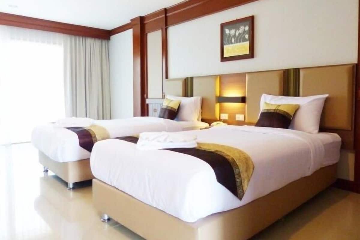 A hotel room with two beds, a large window with curtains, a framed picture on the wall, and a wooden headboard.