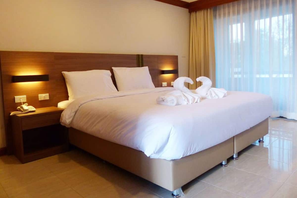 A hotel room with a large bed, a bedside table with a phone, and a window with sheer curtains.