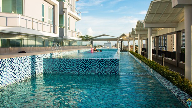 Une piscine dont les bords sont recouverts de carreaux, entourée de bâtiments modernes dotés de balcons et de grandes fenêtres.