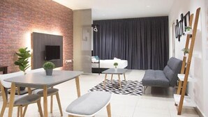 Un salon moderne avec un mur d’accent en briques, un coin repas avec une table et des chaises, un canapé gris et un tapis noir et blanc.
