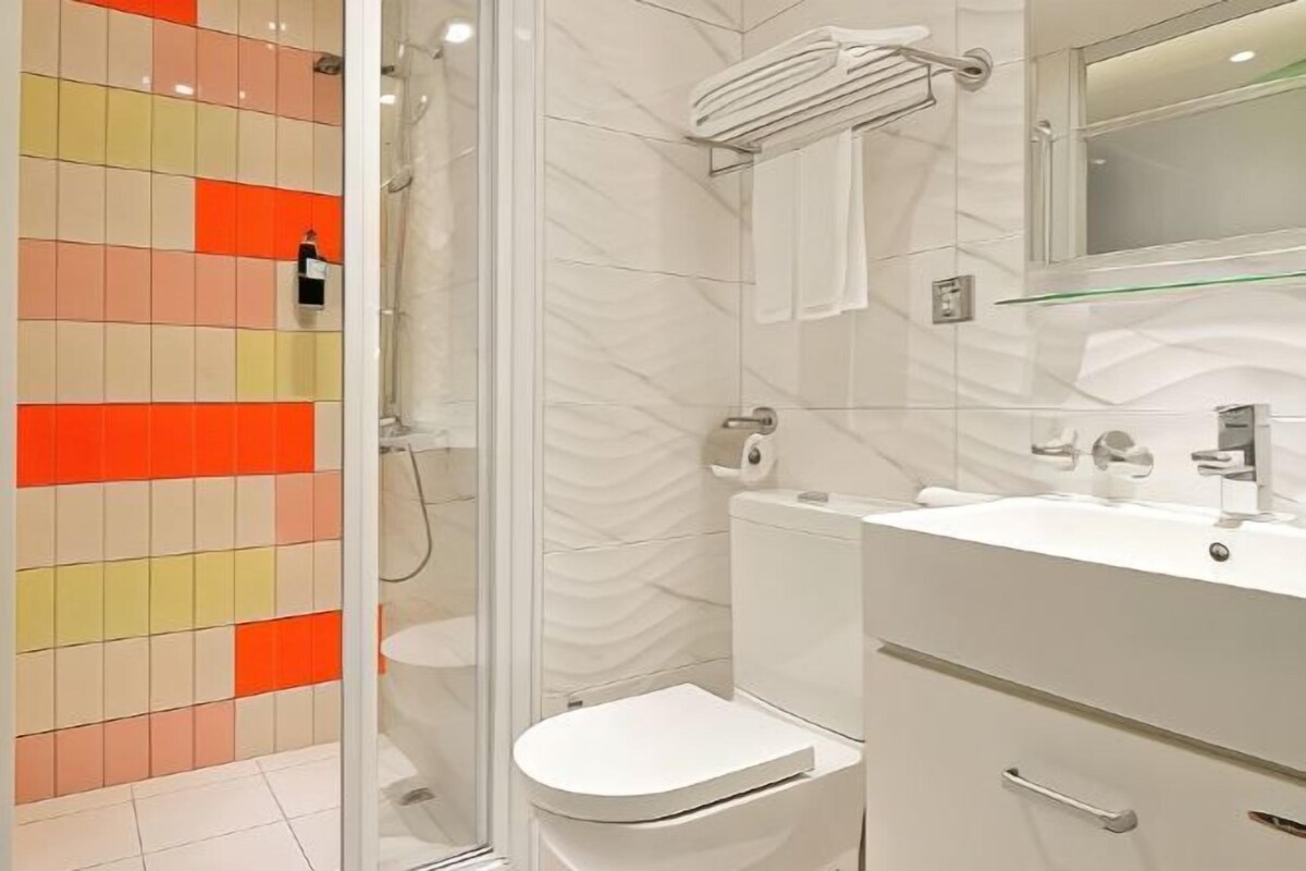 A modern bathroom with a glass shower enclosure, a white toilet, and a vanity with a mirror.