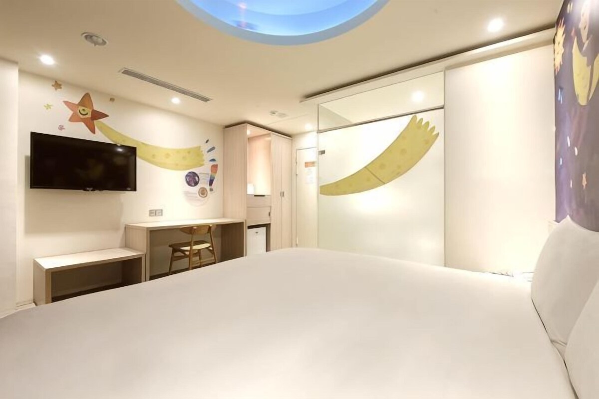 A bedroom with a bed, a desk, a chair, a television, and a wall with a star design.