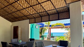 An outdoor patio with wicker furniture, a clock, and a view of the sea. - Bamboo Paradise Beach Resort (Argao)