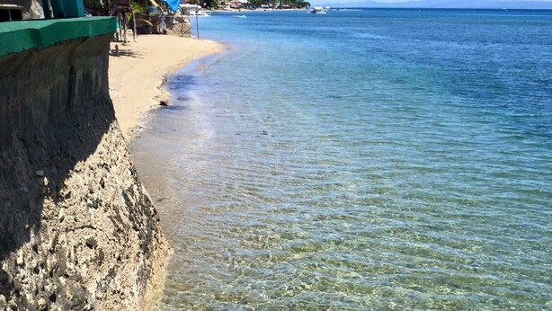A beach with clear shallow waters and a rocky shoreline. - Bamboo Paradise Beach Resort (Argao)