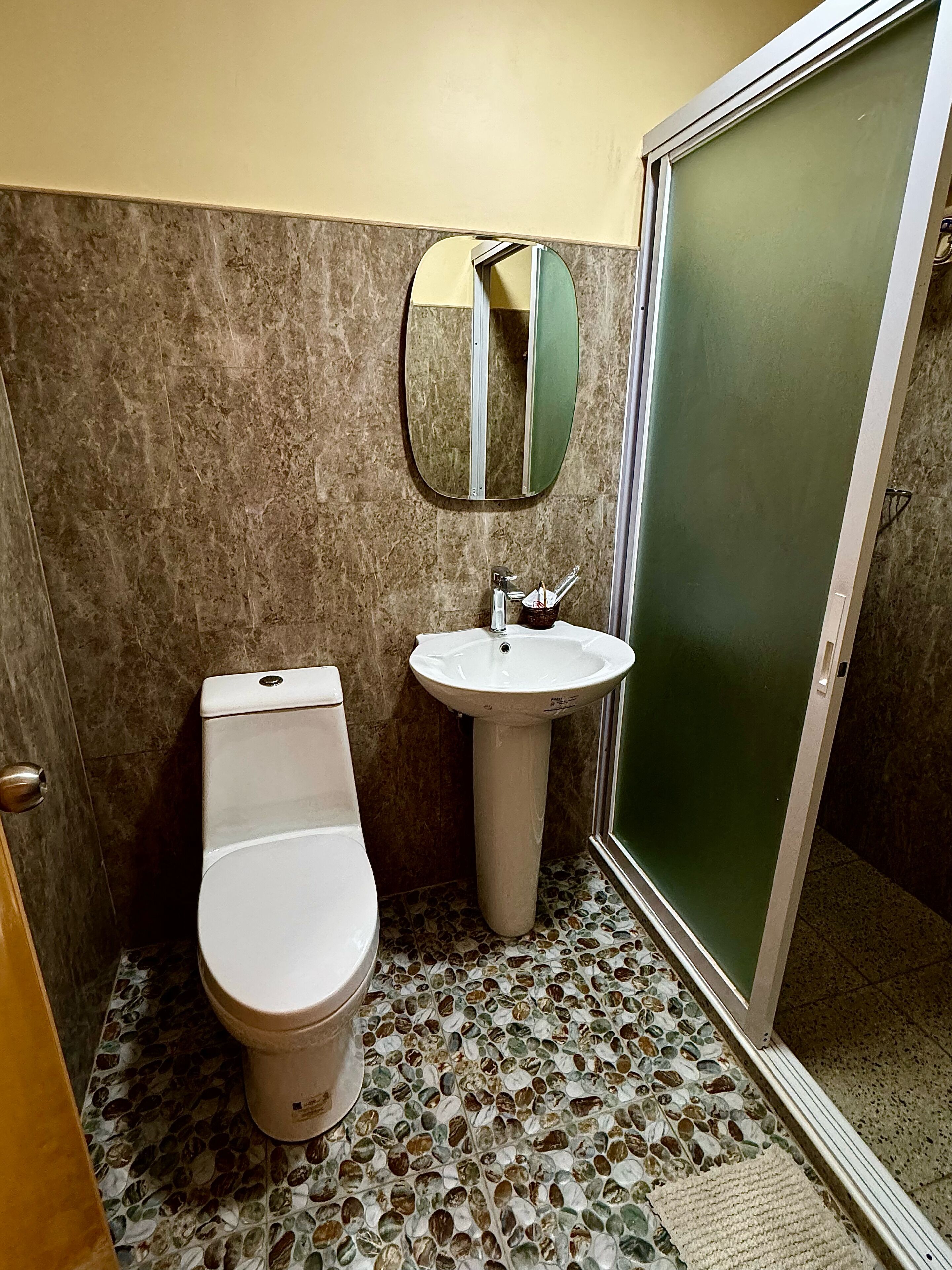 Casa de banho com sanita, lavatório e chuveiro com porta de vidro.