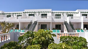 A white building with multiple balconies, green railings, and a staircase leading to the upper floors. - Apartamentos Tisalaya (Tías)
