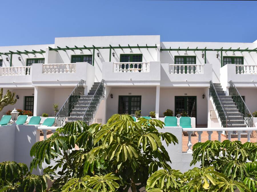 Um edifício branco com várias varandas, grades verdes e uma escadaria que leva aos andares superiores.