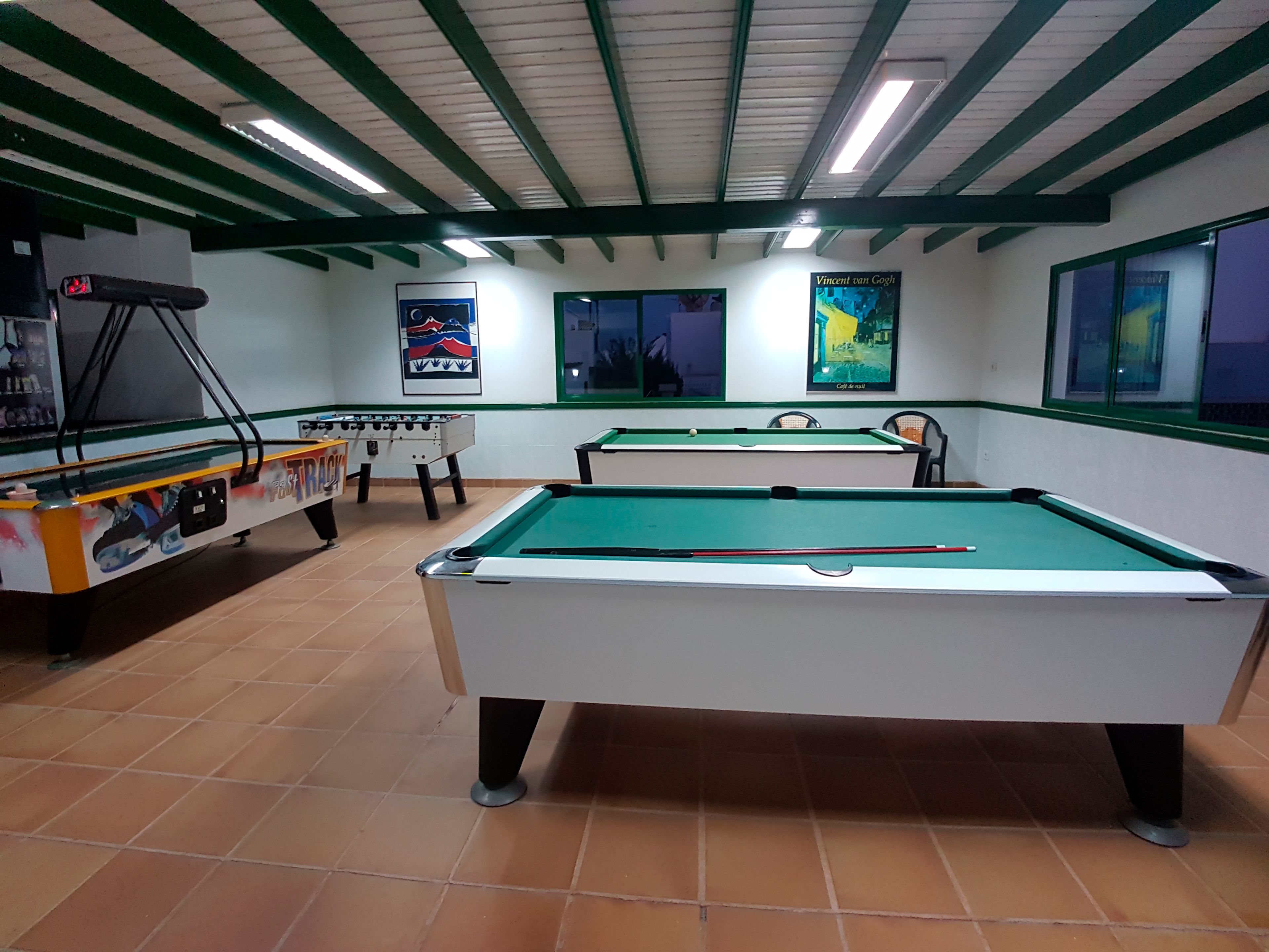 A billiards room with two pool tables, a foosball table, and a poster of Vincent van Gogh.