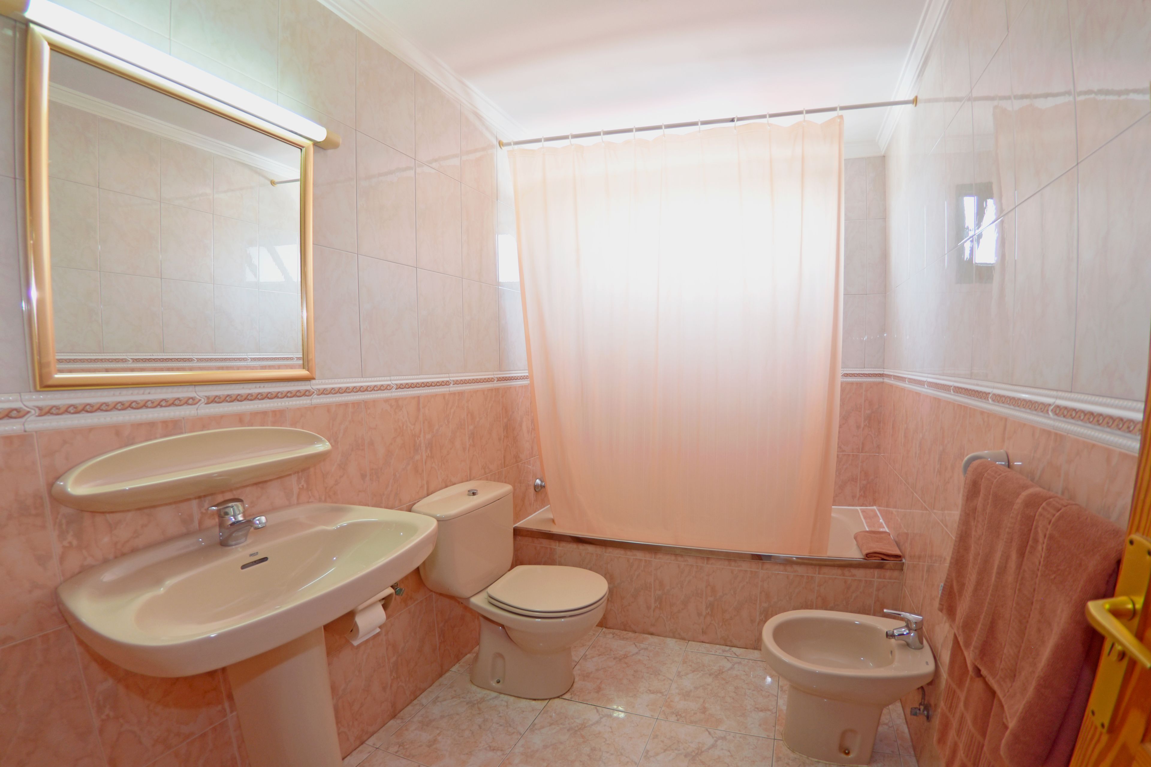 Et badeværelse med vask, toilet, bidet og bruseforhæng.