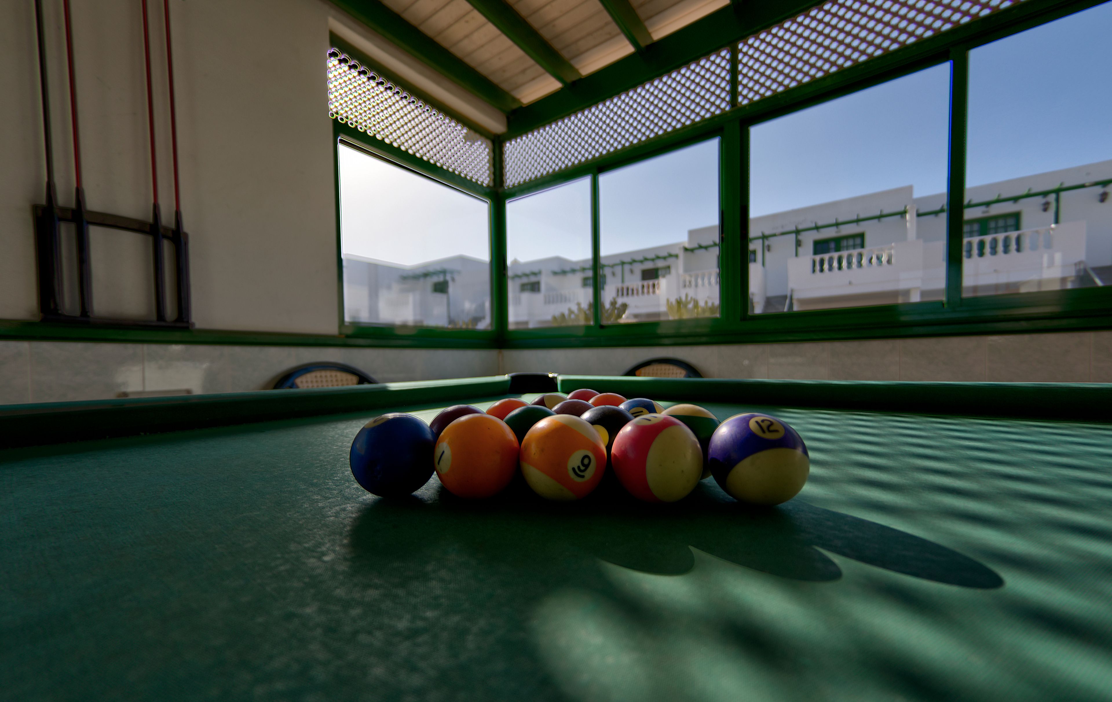 A pool table with balls in a room with large windows and a view of buildings outside.