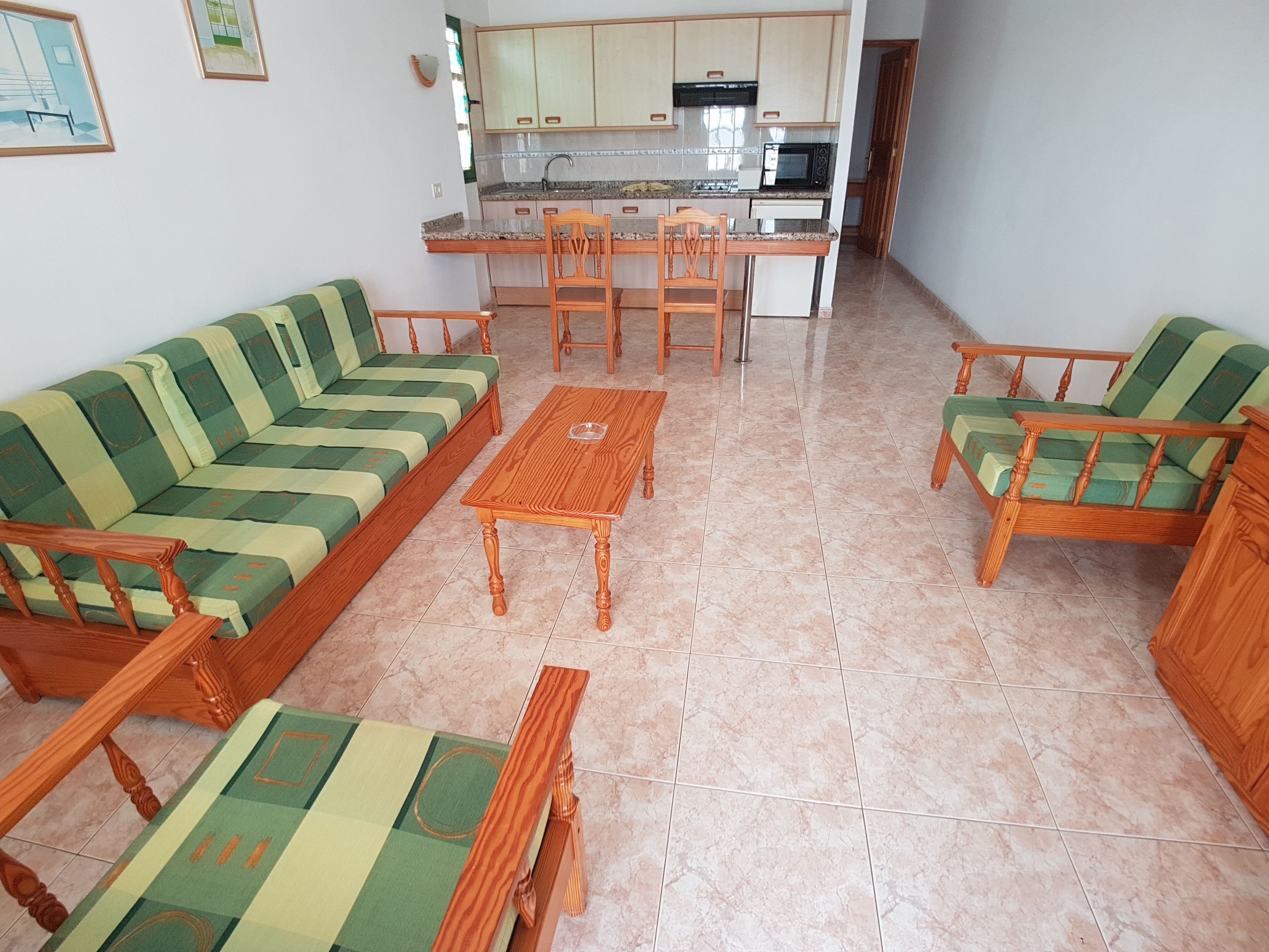 Una sala de estar con sofá, sillas, una mesita de centro y una cocina al fondo.