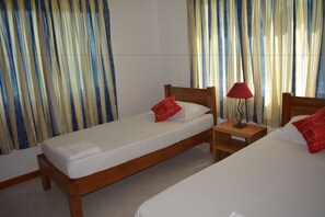 A hotel room with two single beds, wooden headboards, a nightstand with a lamp, and striped curtains.