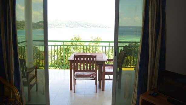 Un balcon avec une table et des chaises, donnant sur une étendue d’eau et sur de la verdure.