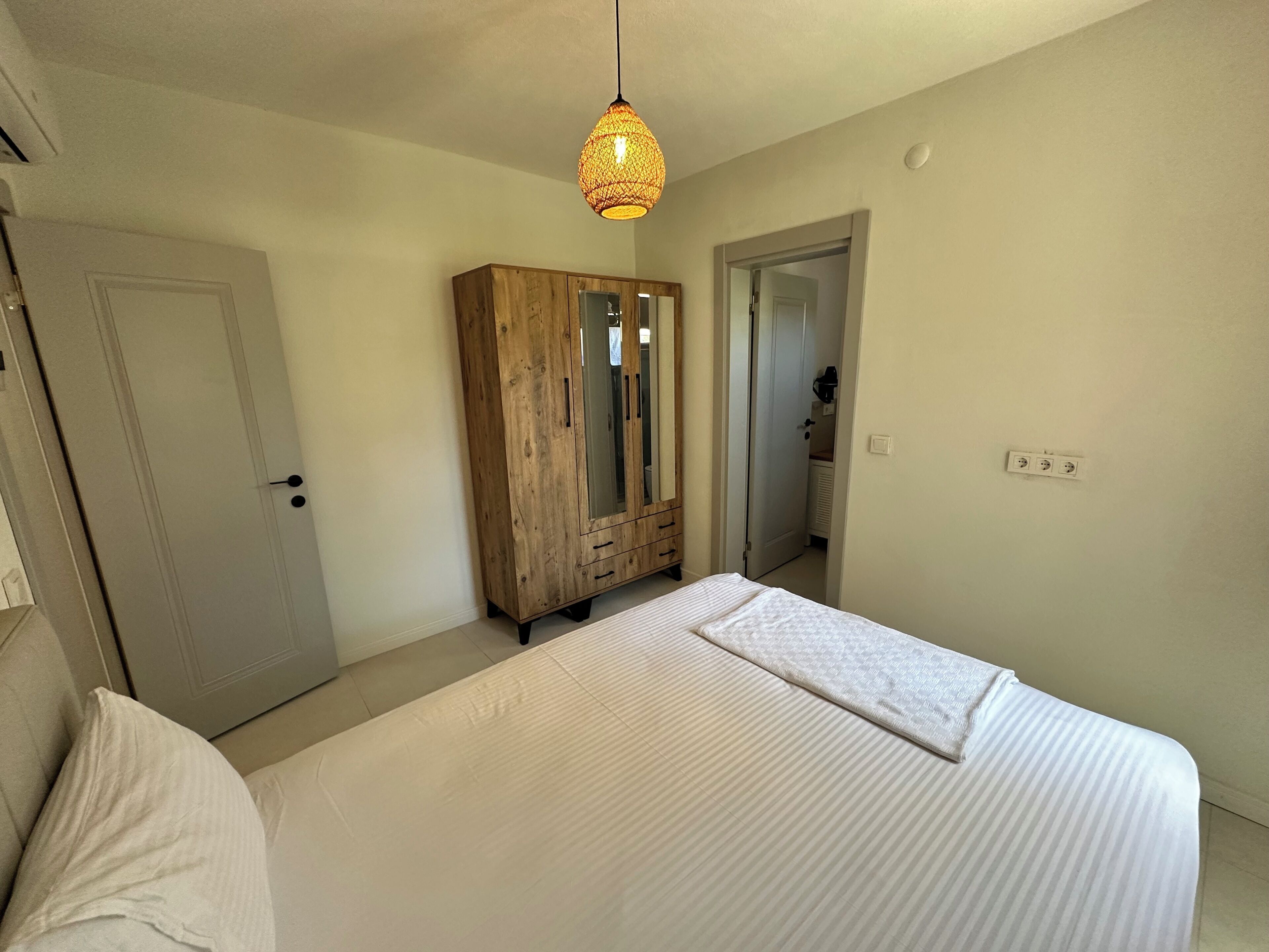 Un dormitorio con cama, armario, espejo y lámpara colgante.