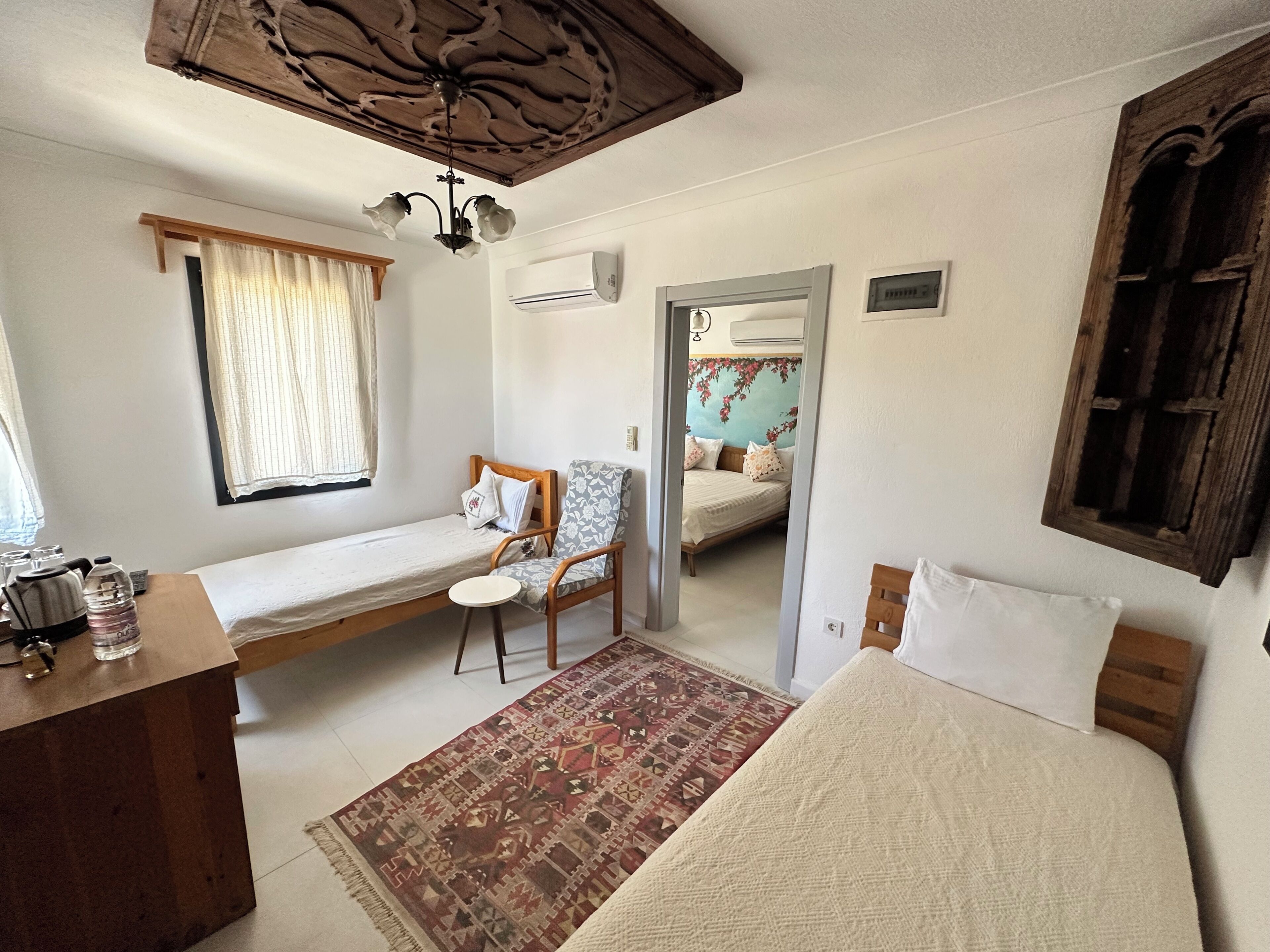 Un dormitorio con una cama individual, una silla, una mesita y un equipo de aire acondicionado, además de un espejo.
