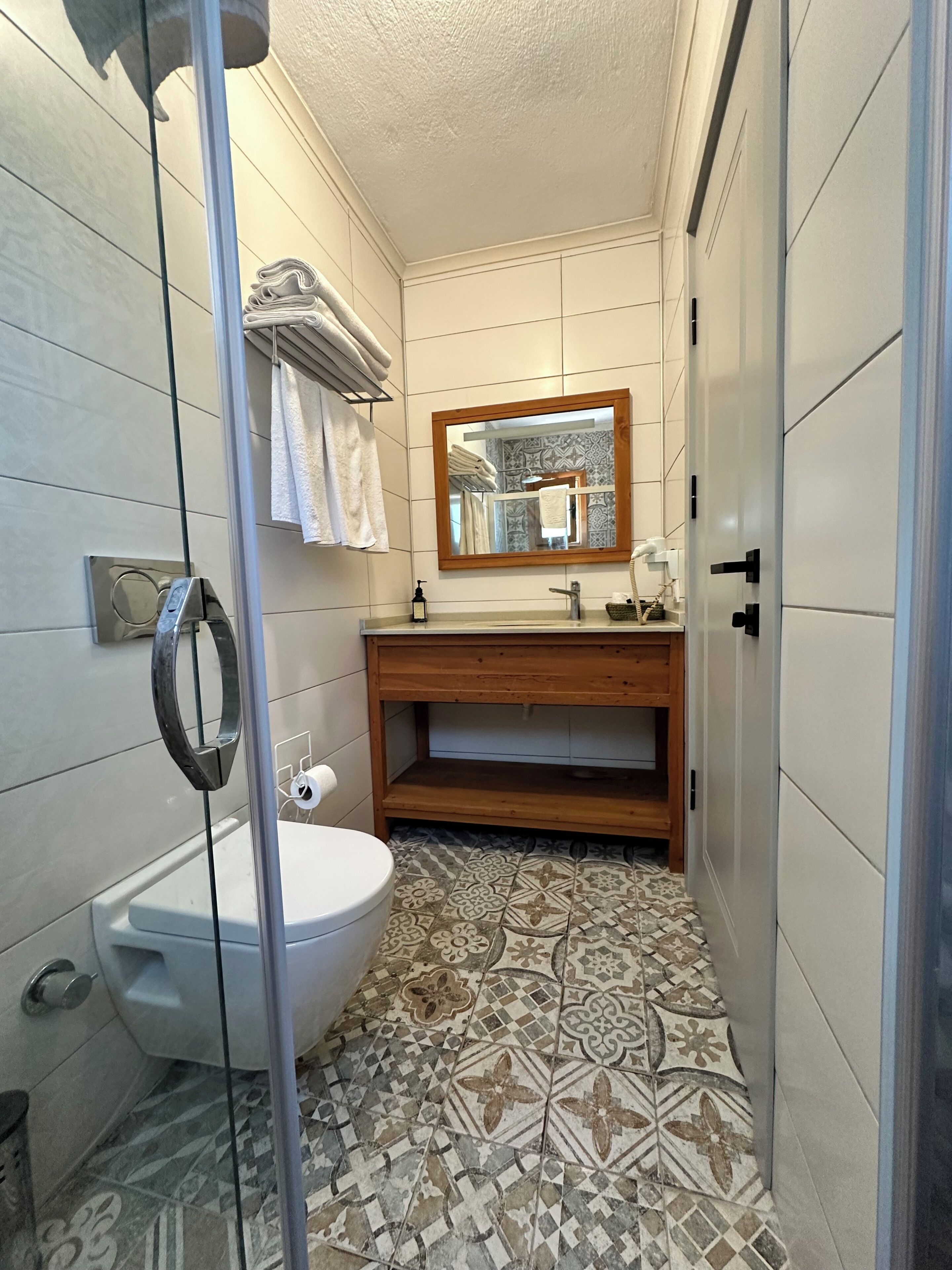 Un baño con cabina de ducha de vidrio, inodoro, lavabo con tocador de madera y baldosas de suelo con diseño.